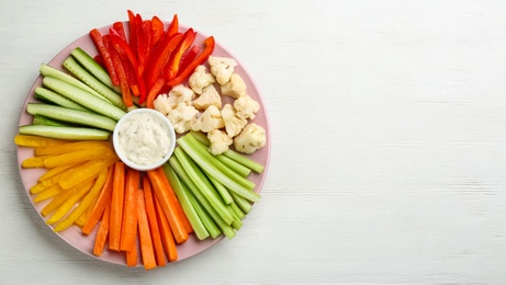 Celery sticks, other vegetables and dip sauce on white wooden table, top view. Space for text