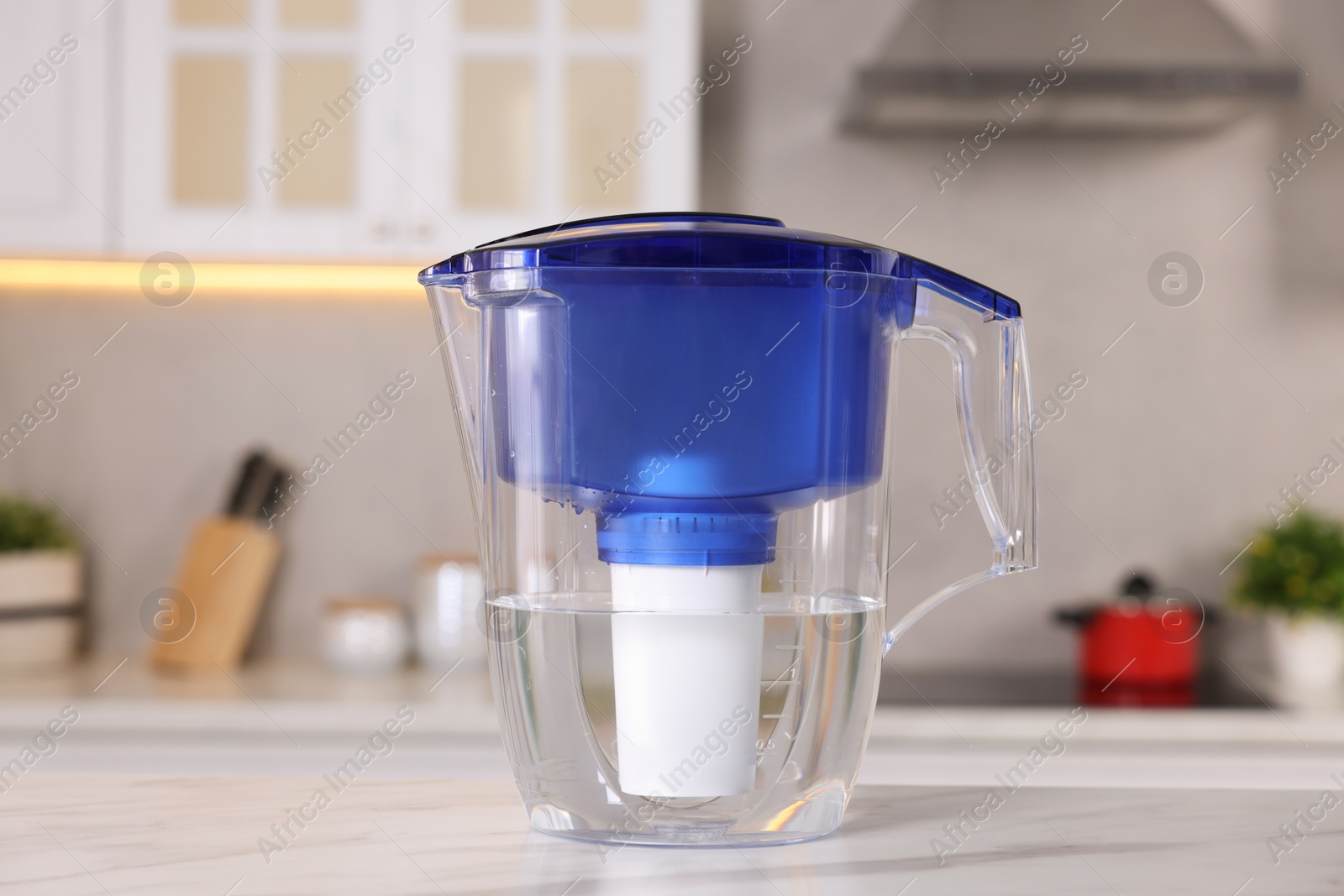 Photo of Water filter jug on white marble table in kitchen, closeup