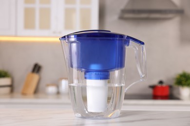 Photo of Water filter jug on white marble table in kitchen, closeup