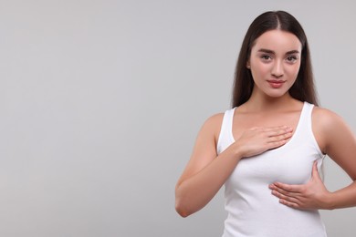 Photo of Beautiful young woman doing breast self-examination on light grey background, space for text