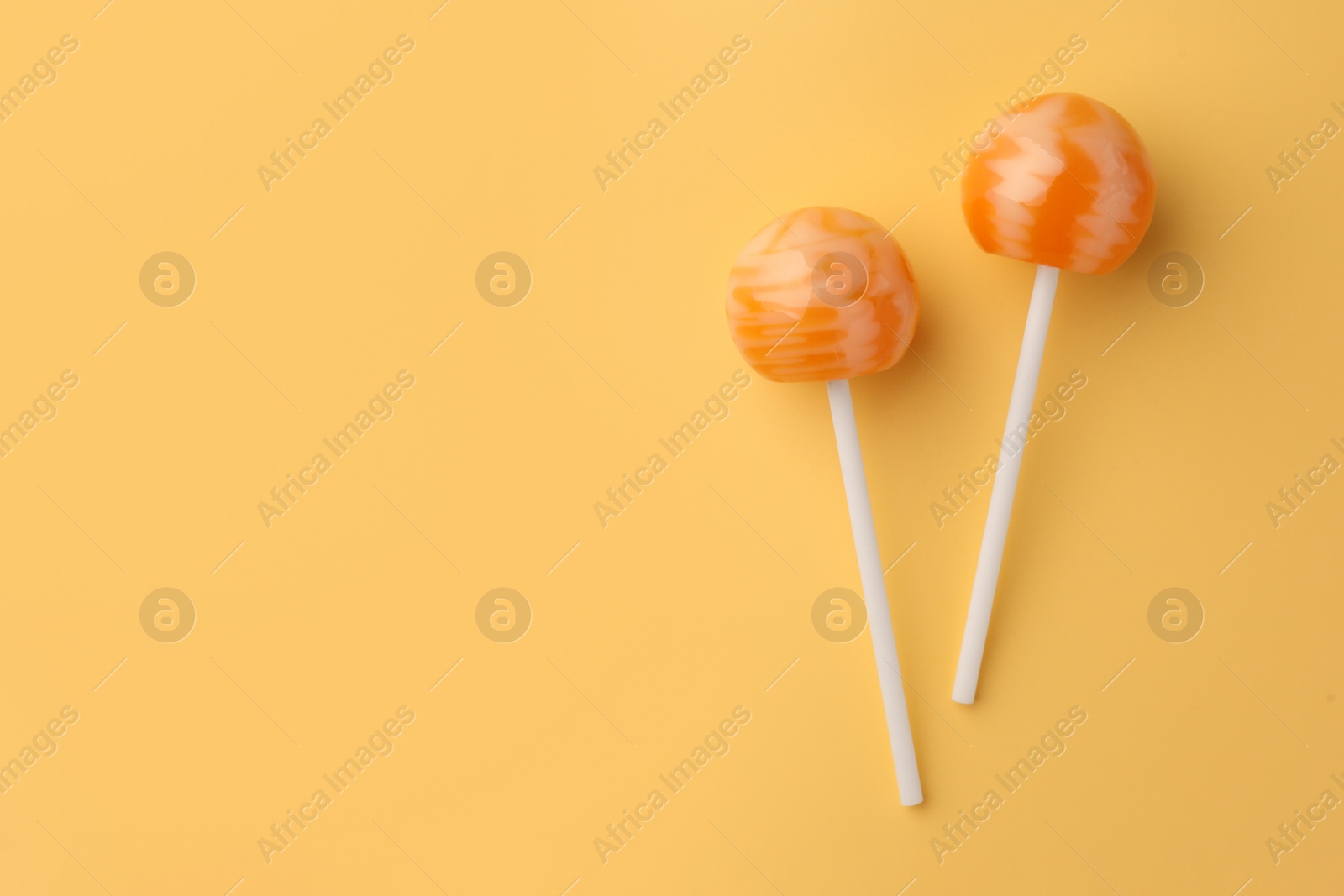 Photo of Tasty lollipops on orange background, flat lay. Space for text