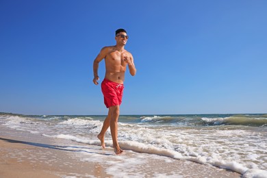 Photo of Handsome man with attractive body running on beach