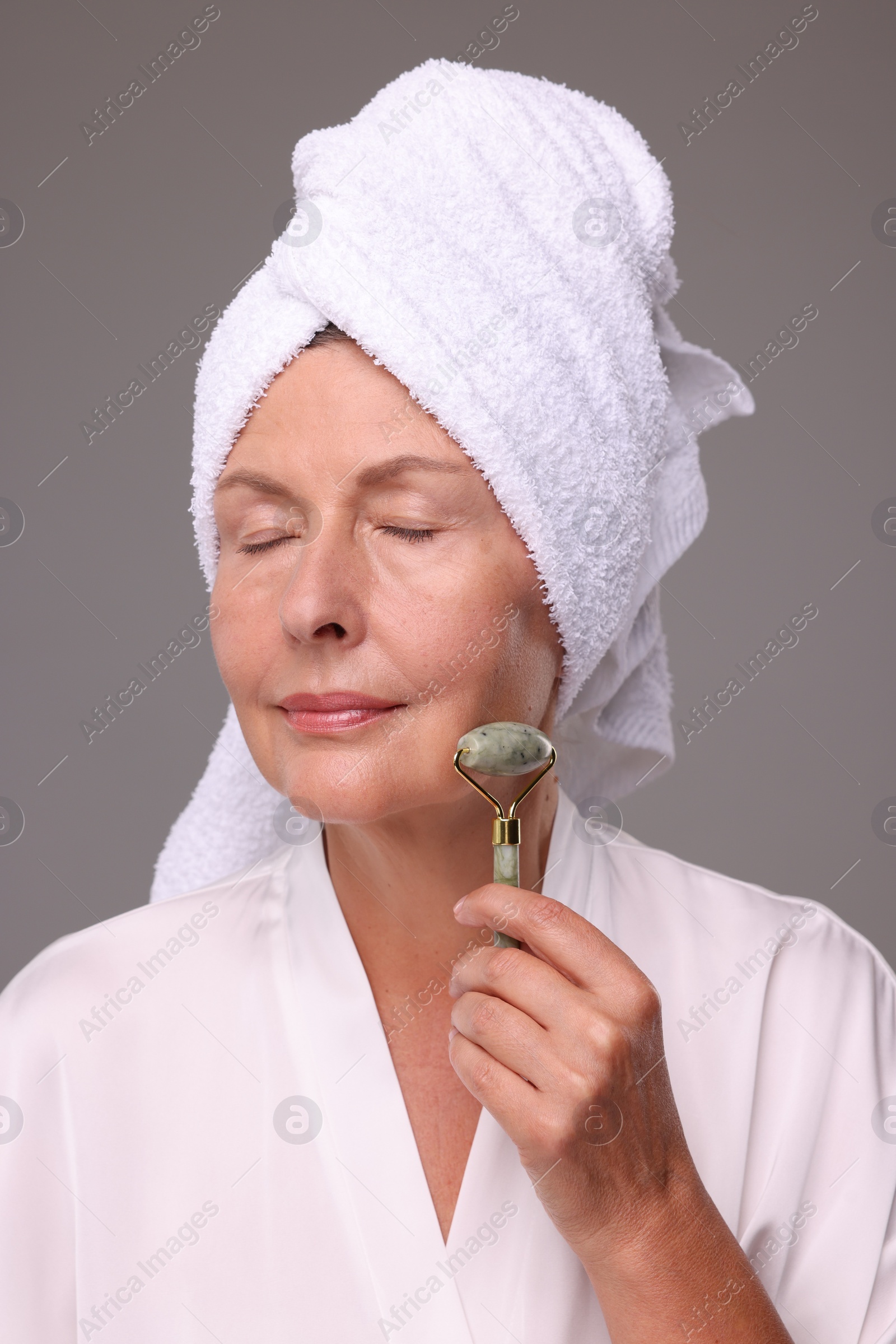 Photo of Woman massaging her face with jade roller on grey background