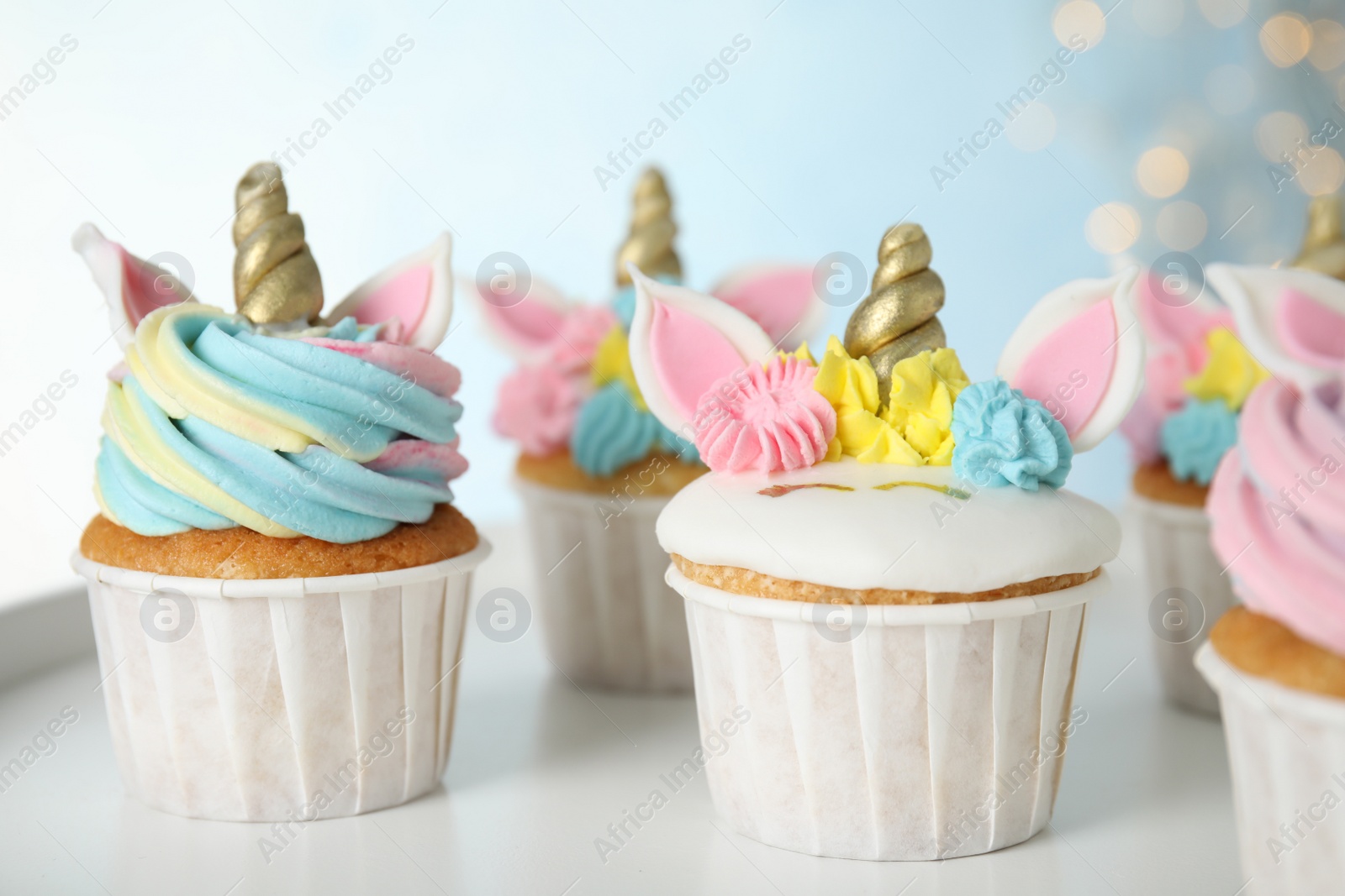 Photo of Many cute sweet unicorn cupcakes on white table