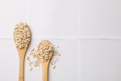 Wooden spoons with dry pearl barley on white tiled table, top view. Space for text