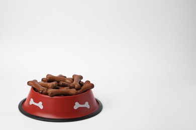 Red bowl with bone shaped dog cookies on white background, space for text