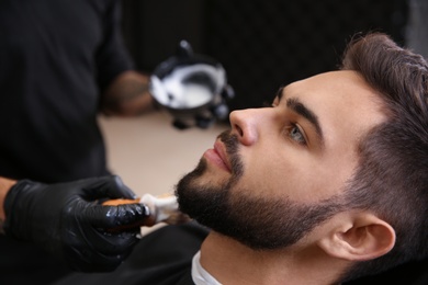 Professional hairdresser applying shaving foam onto client's skin in barbershop