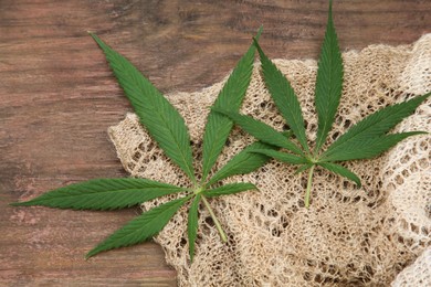 Photo of Hemp cloth and green leaves on wooden table, top view