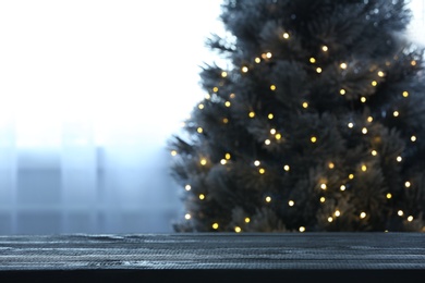 Photo of Blurred view of beautiful Christmas tree with yellow lights near window indoors, focus on wooden table. Space for text