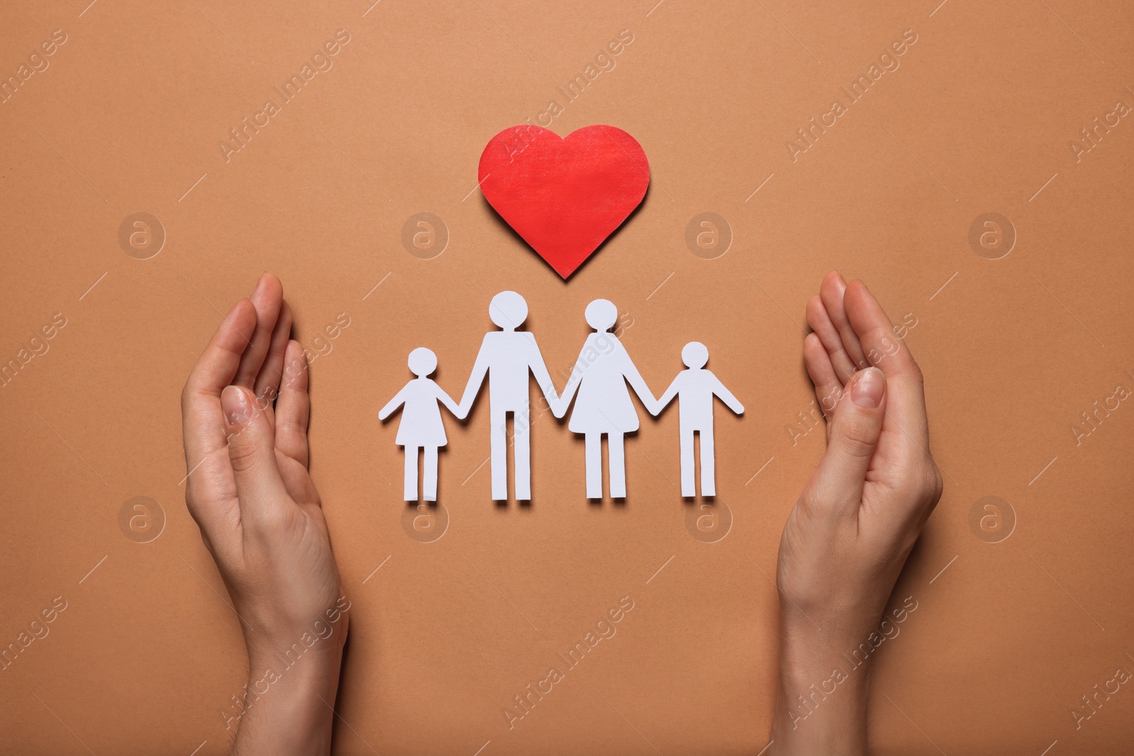 Photo of Woman protecting paper family figures and red heart on brown background, top view. Insurance concept