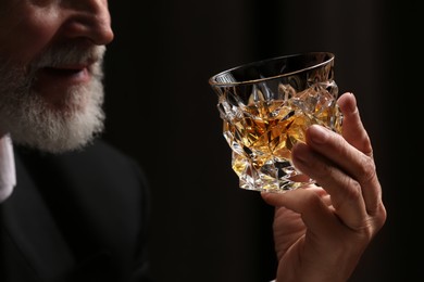 Photo of Man holding glass of whiskey with ice cubes on dark background, closeup