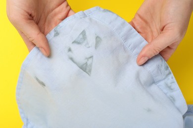 Woman showing shirt with stain on yellow background, top view