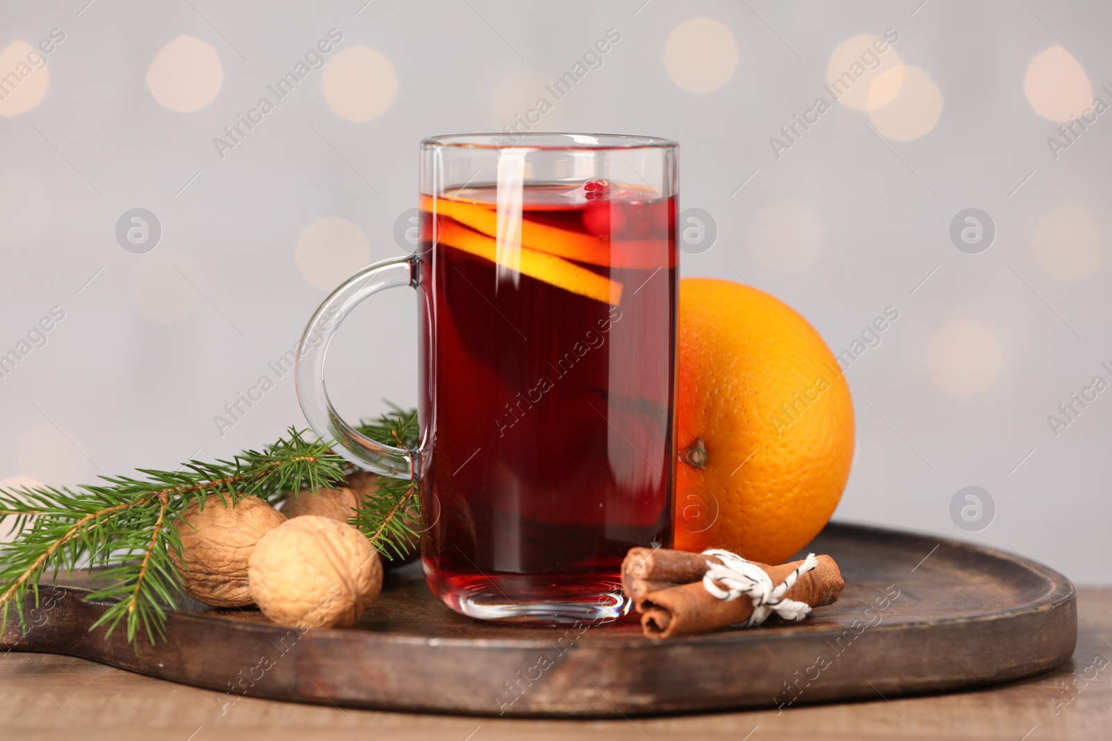 Photo of Aromatic mulled wine in glass cup on wooden table against grey background with blurred lights, closeup