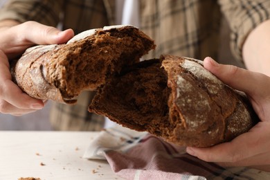 Man breaking loaf of fresh bread on white table, closeup