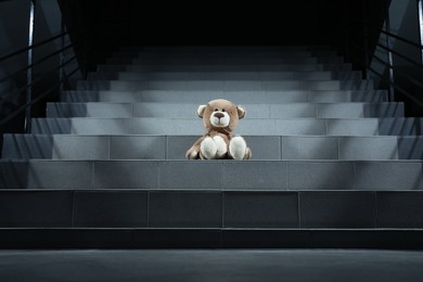 Photo of Lonely teddy bear on grey stairs indoors, low angle view