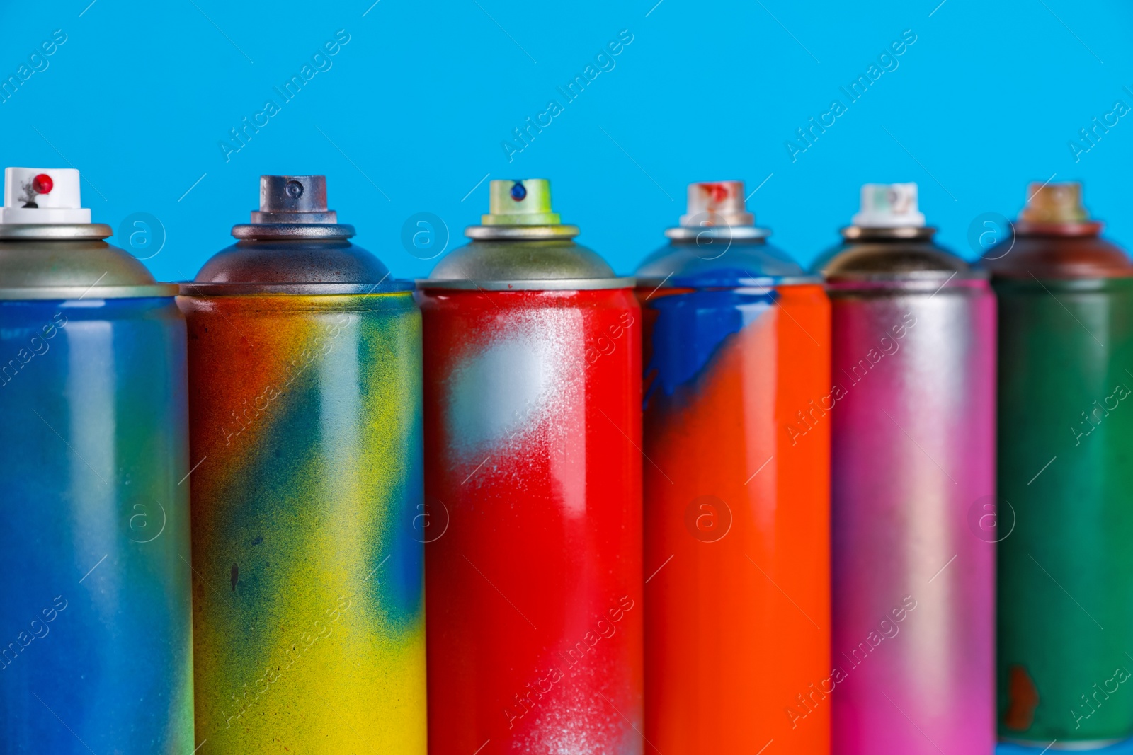 Photo of Used cans of spray paints on light blue background, closeup