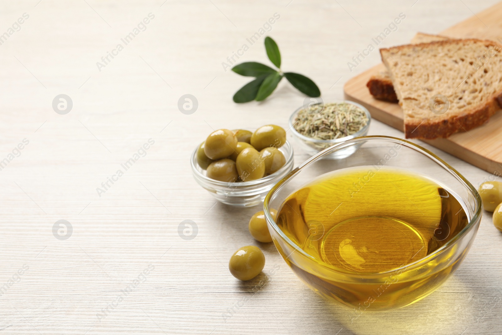 Photo of Glass bowl with fresh olive oil on white wooden table, space for text