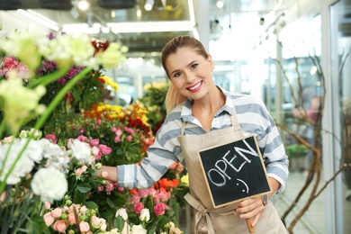 Photo of Female florist holding sign "OPEN" in flower shop