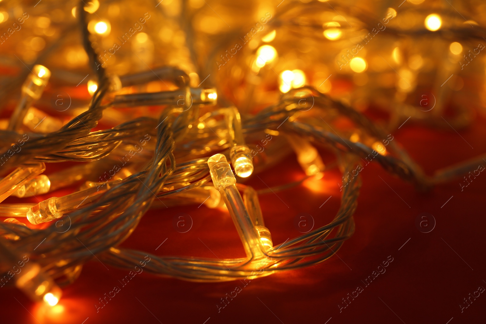 Photo of Glowing Christmas lights on red background, closeup