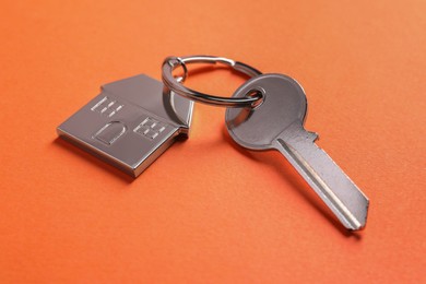 Metallic key with keychain in shape of house on orange background