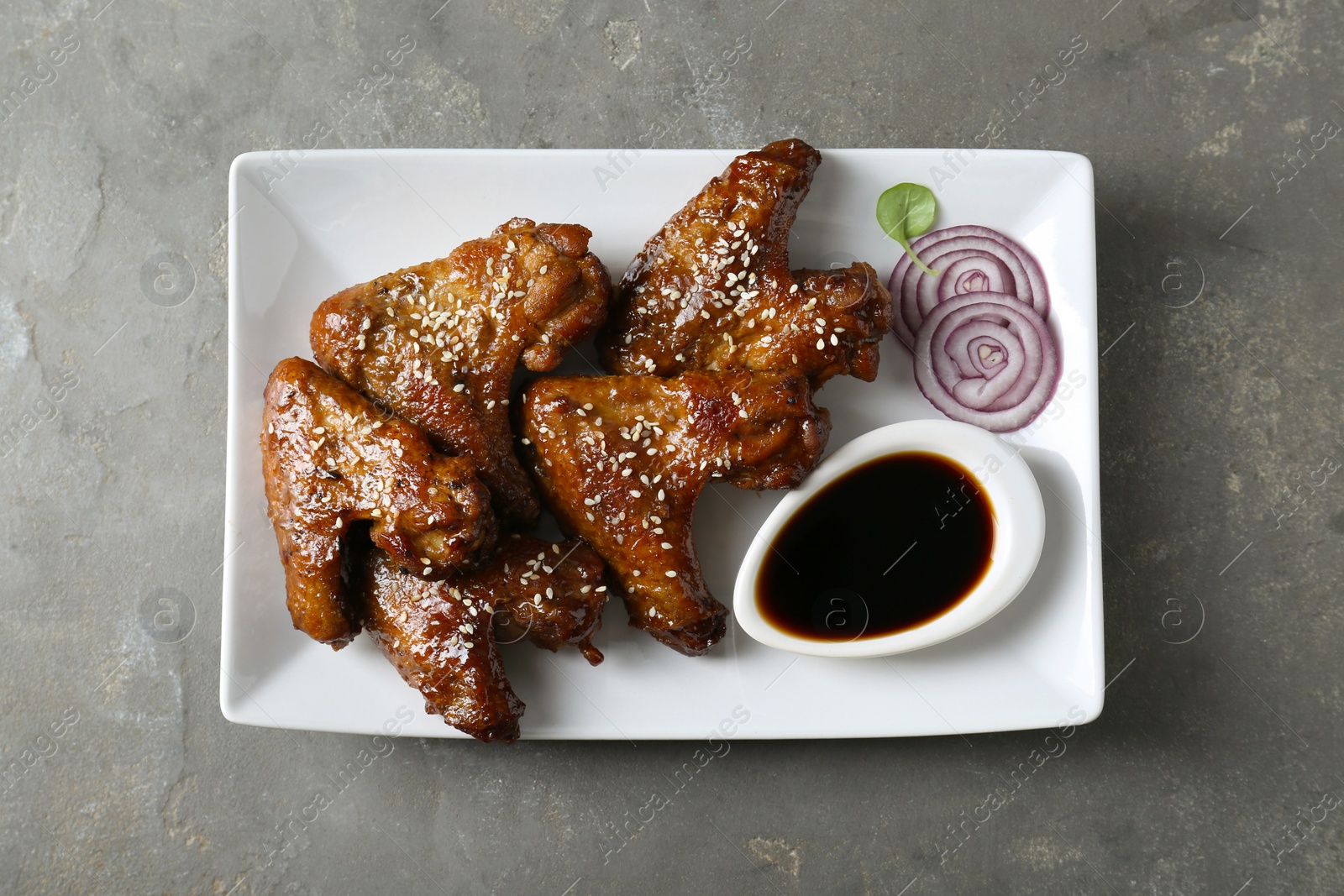 Photo of Glazed chicken wings and soy sauce on grey table, top view