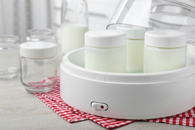 Photo of Modern yogurt maker and jars on wooden table in kitchen