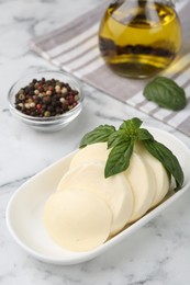 Photo of Plate with tasty mozzarella slices and basil leaves on white marble table