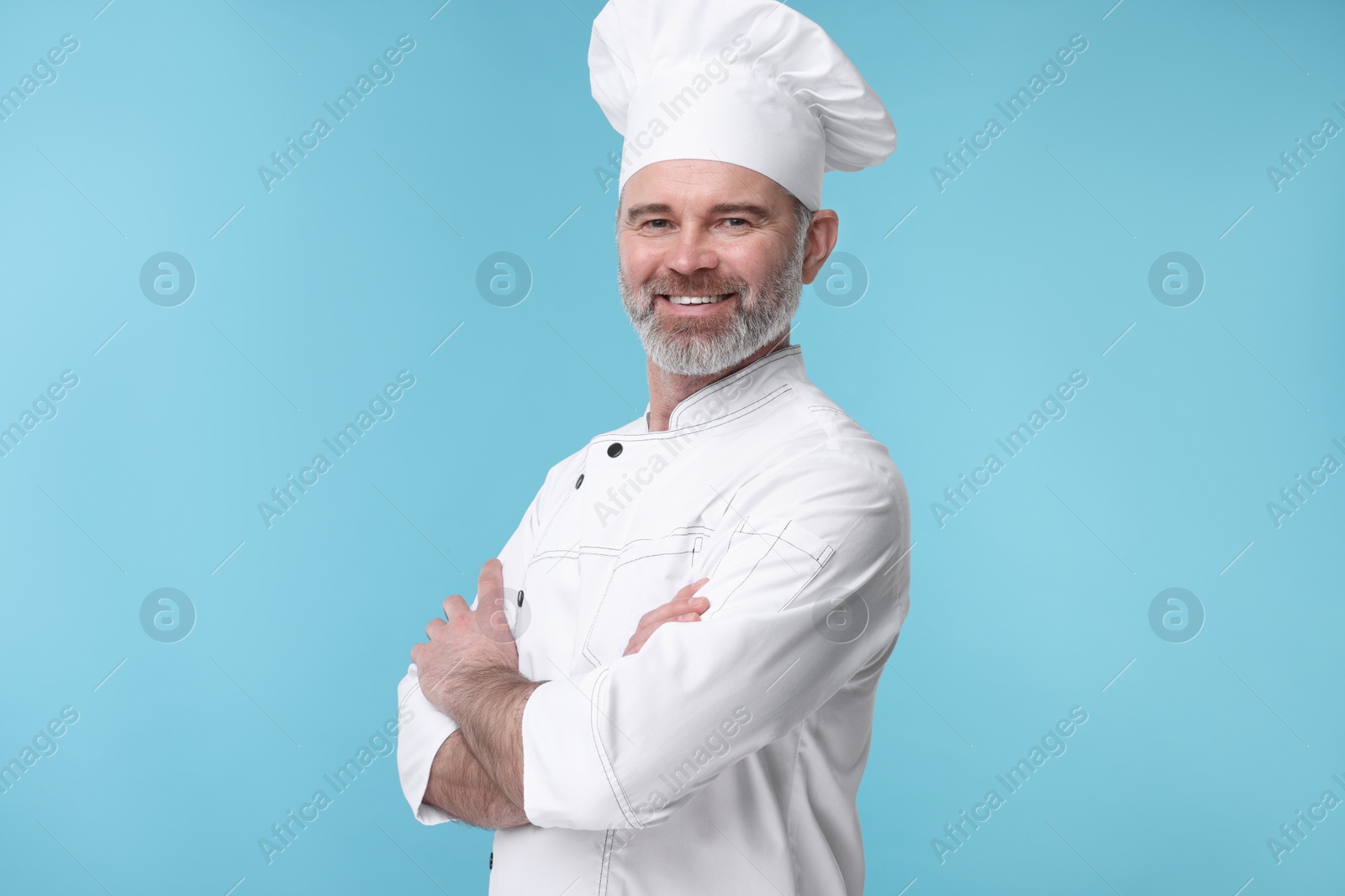 Photo of Happy chef in uniform on light blue background