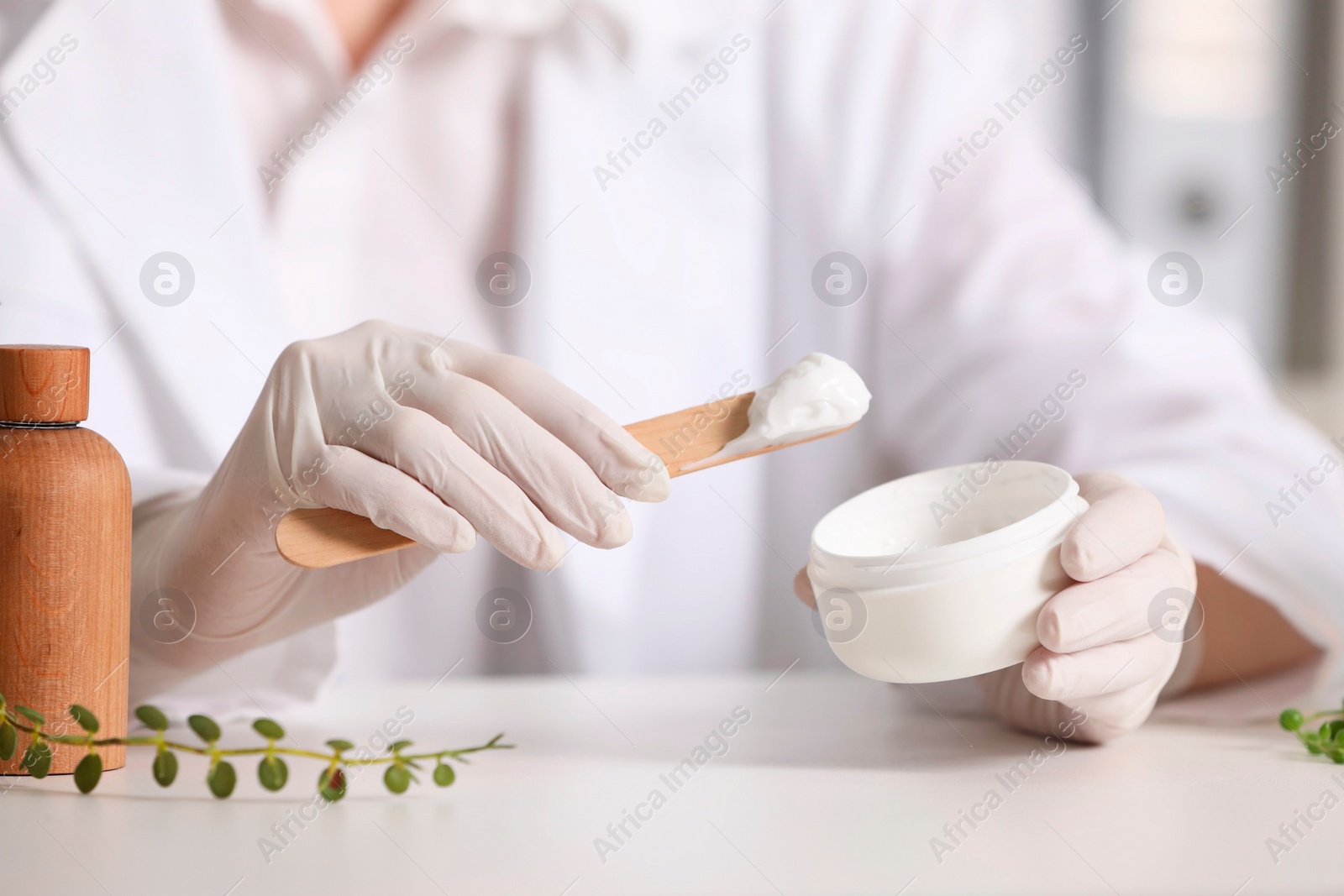 Photo of Dermatologist with jar testing cosmetic product at white table indoors, selective focus