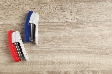 Photo of Color staplers on wooden table, flat lay. Space for text