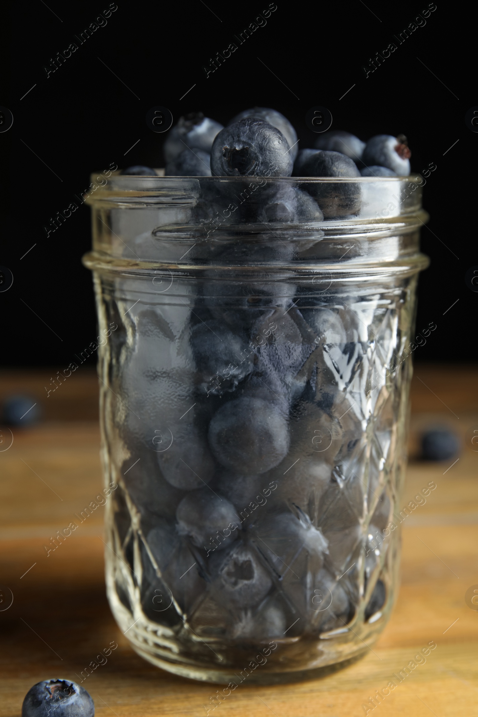 Photo of Tasty ripe blueberries in glass jar on wooden table