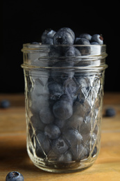 Photo of Tasty ripe blueberries in glass jar on wooden table