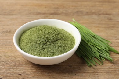 Photo of Wheat grass powder in bowl and fresh green sprouts on wooden table, closeup