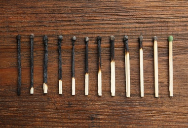 Photo of Row of burnt matches and whole one on wooden background, flat lay. Human life phases concept