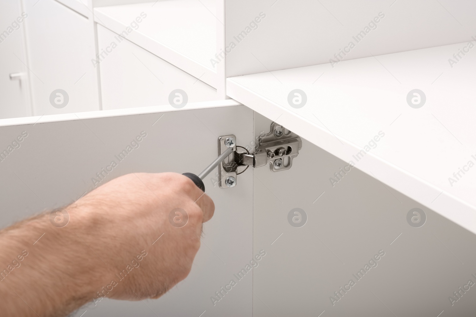 Photo of Man fixing door of white wardrobe with screwdriver, closeup