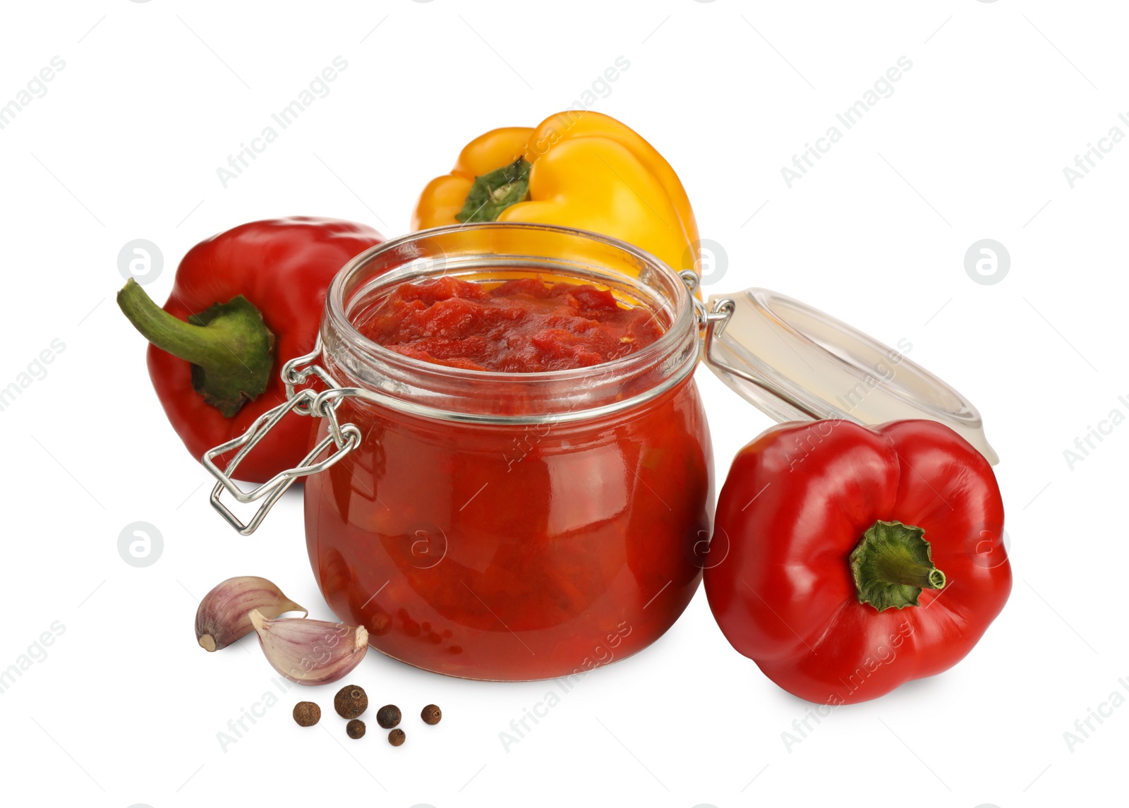 Photo of Glass jar of delicious canned lecho, fresh vegetables and peppercorns on white background