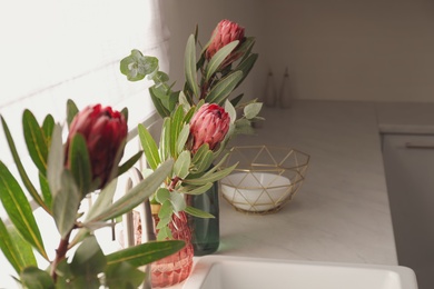 Beautiful protea flowers on countertop near window in kitchen, space for text. Interior design