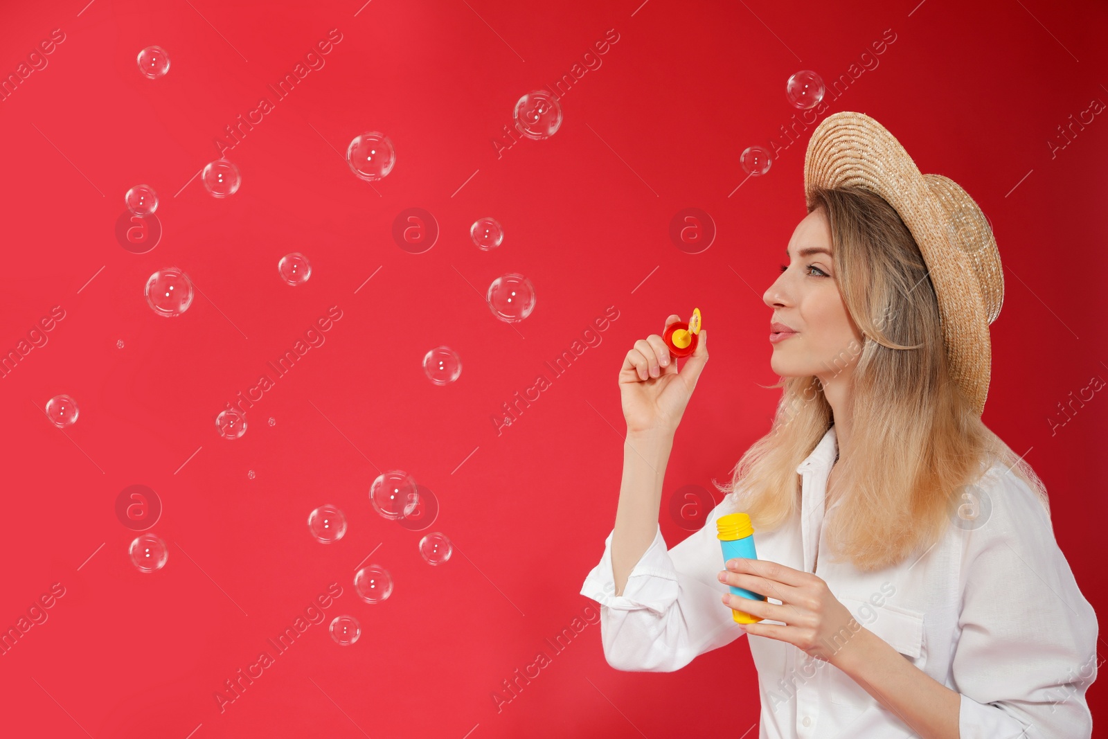 Photo of Young woman blowing soap bubbles on red background, space for text