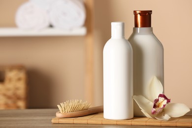 Bottles of shampoo and flower on wooden table in bathroom, space for text