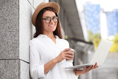 Photo of Beautiful woman with cup of coffee using laptop on city street