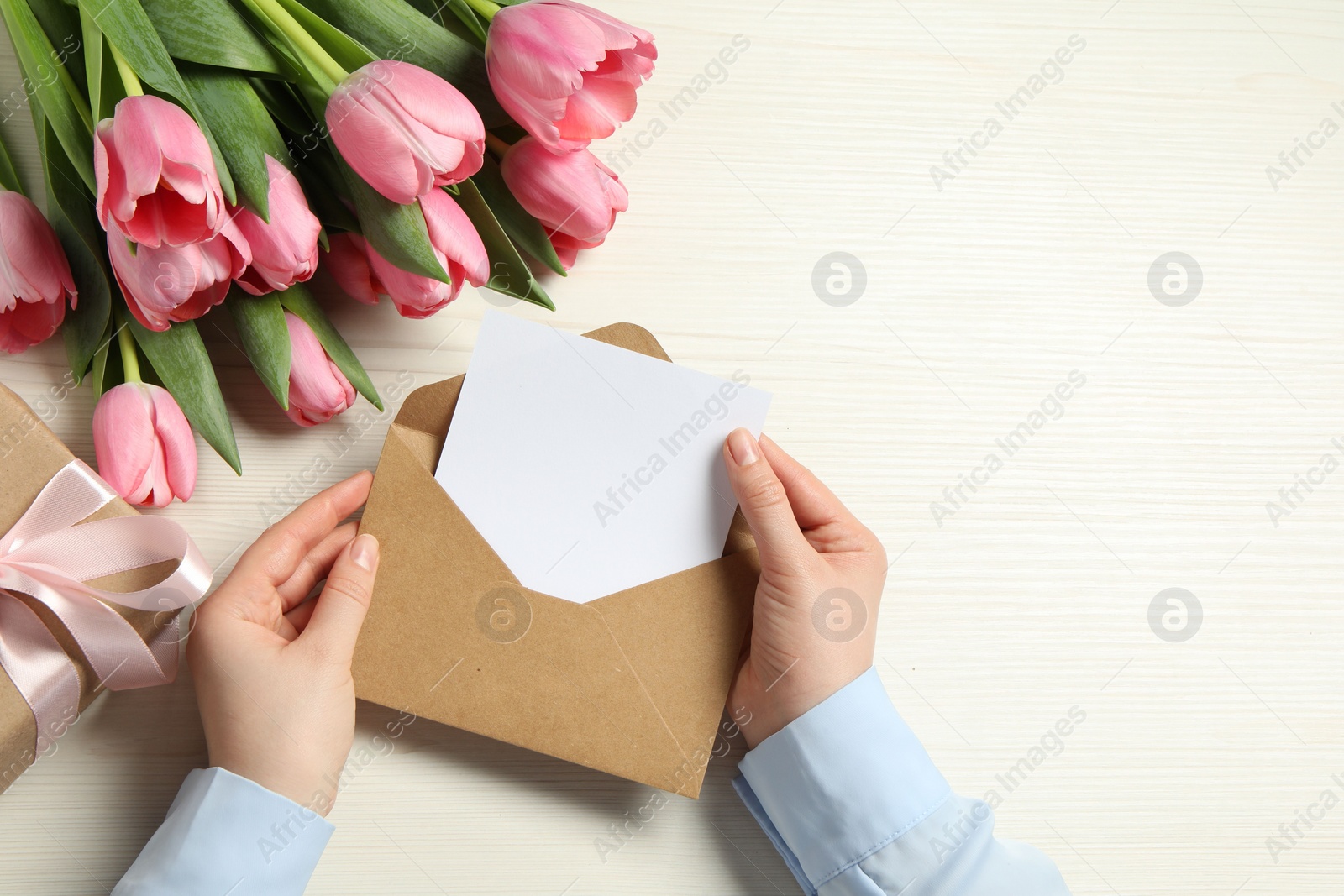 Photo of Happy Mother's Day. Woman holding envelope with blank card at white wooden table, top view. Space for text