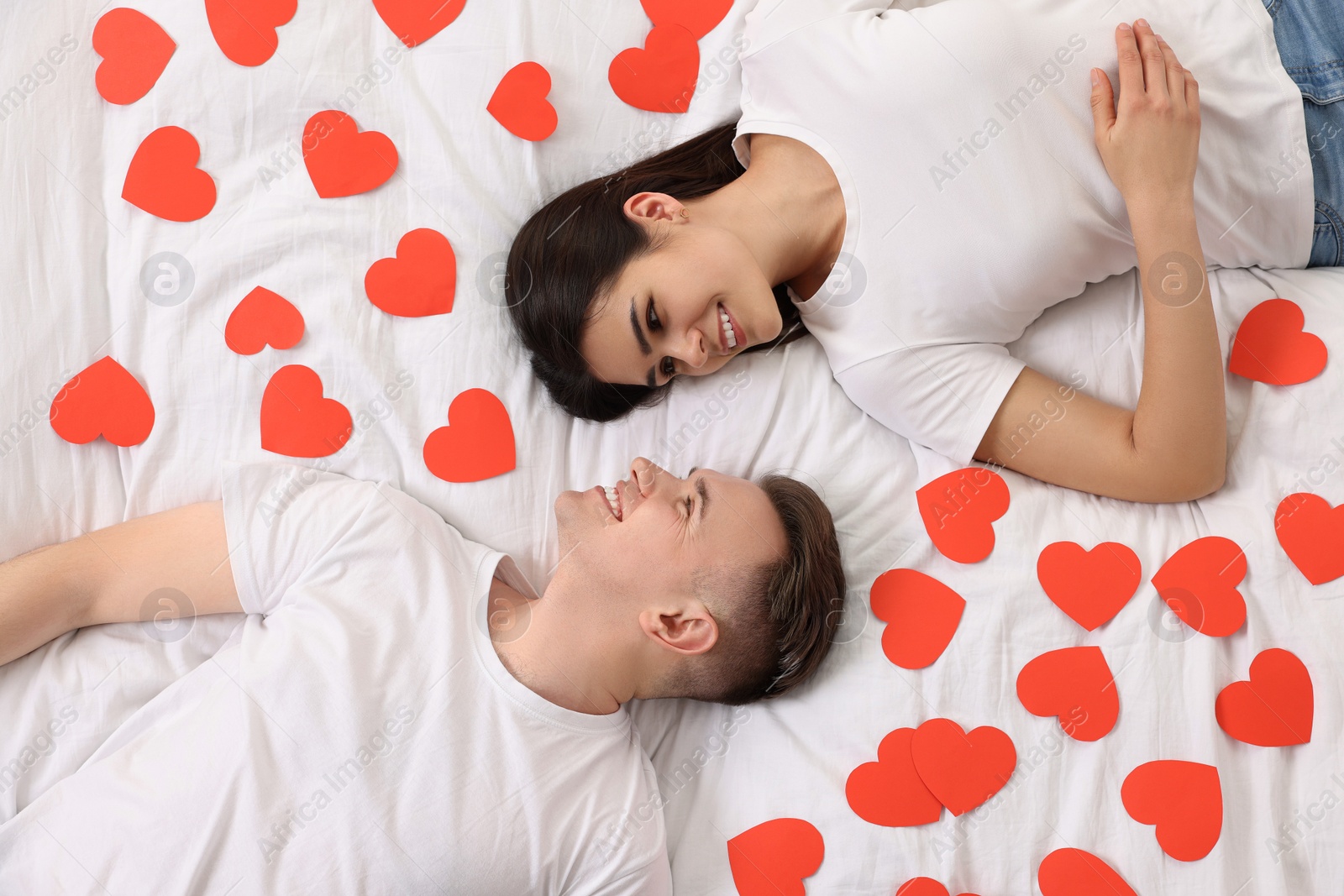 Photo of Lovely couple on bed with many decorative hearts, top view. Valentine's day celebration