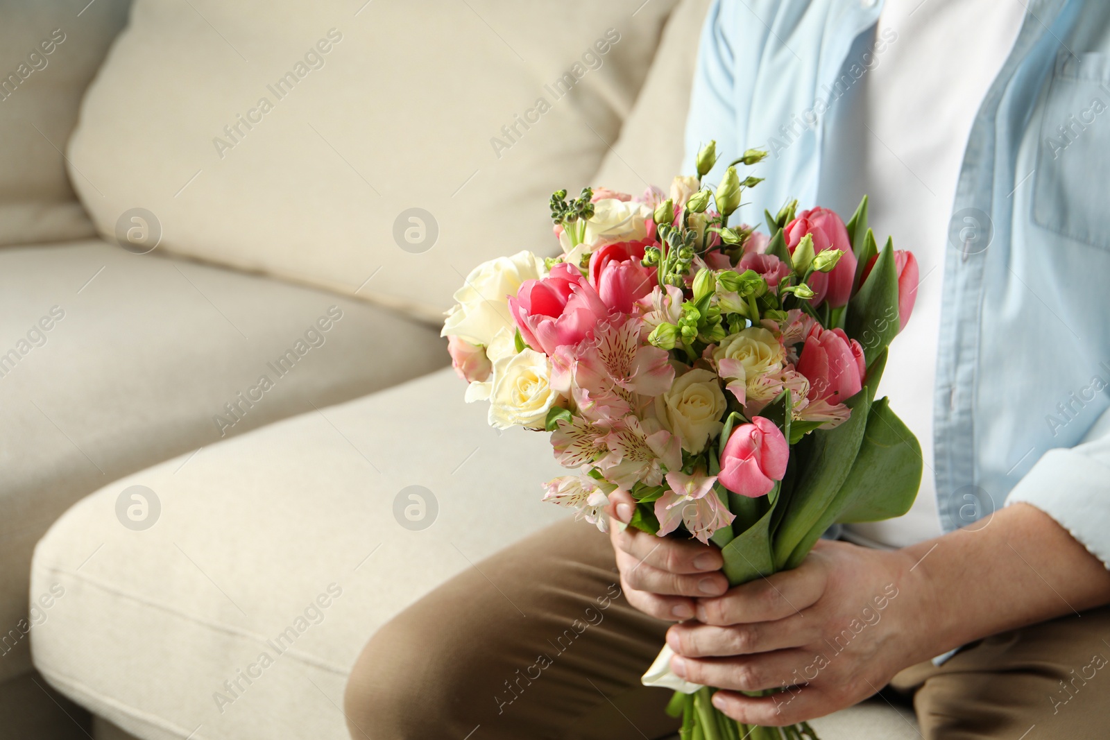 Photo of Man holding bouquet of beautiful flowers indoors, closeup