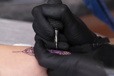 Photo of Professional artist making tattoo on hand, closeup