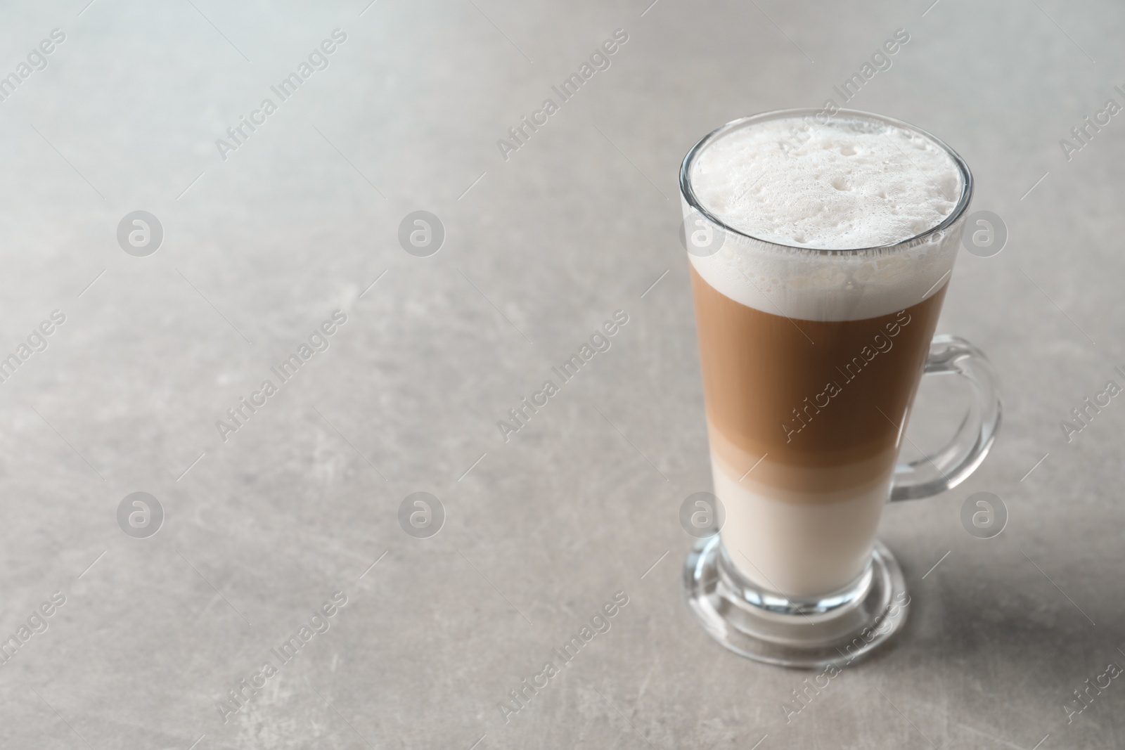 Photo of Glass cup of delicious layered coffee on light grey table, space for text