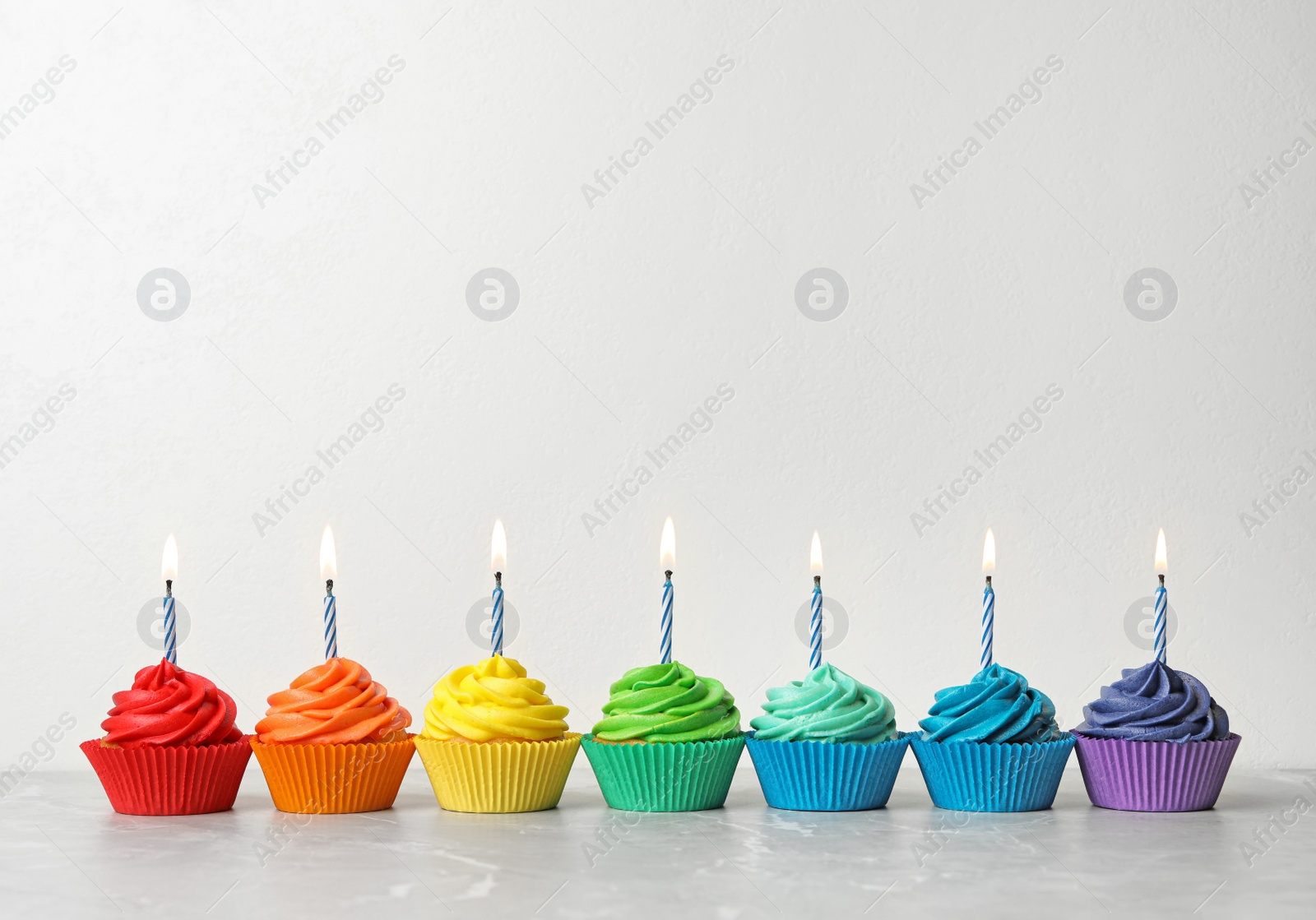 Photo of Delicious birthday cupcakes with burning candles on table