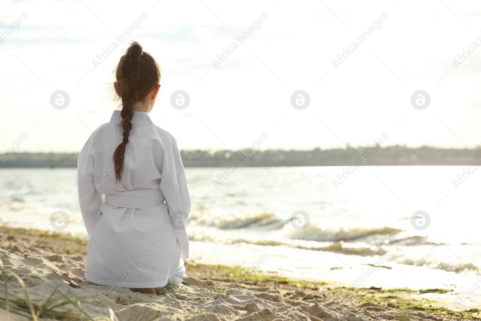 Photo of Cute little girl in kimono meditating outdoors, back view. Karate practicing