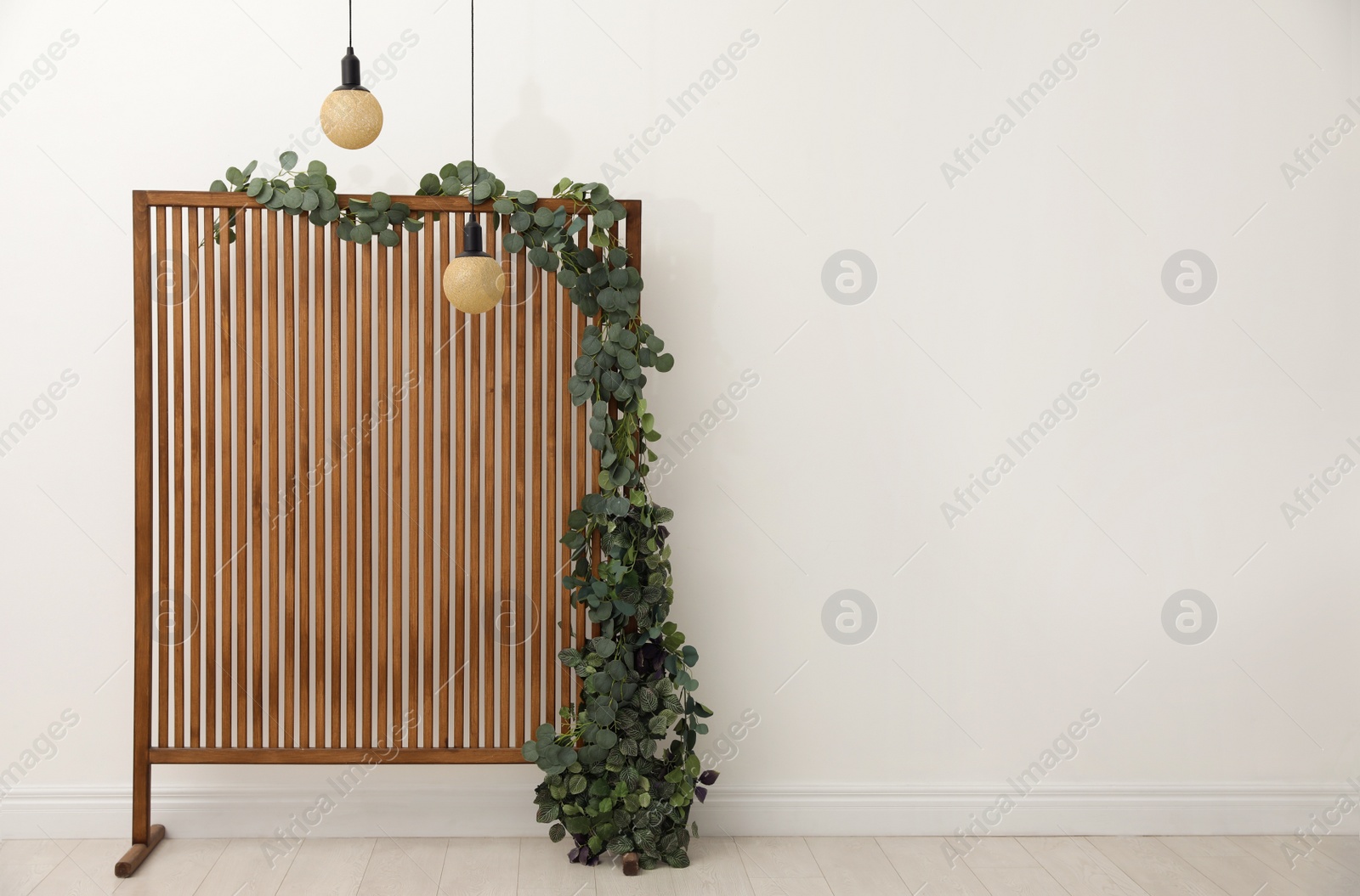 Photo of Stylish photo zone with wooden screen, floral decor and pendant lamps indoors. Space for text