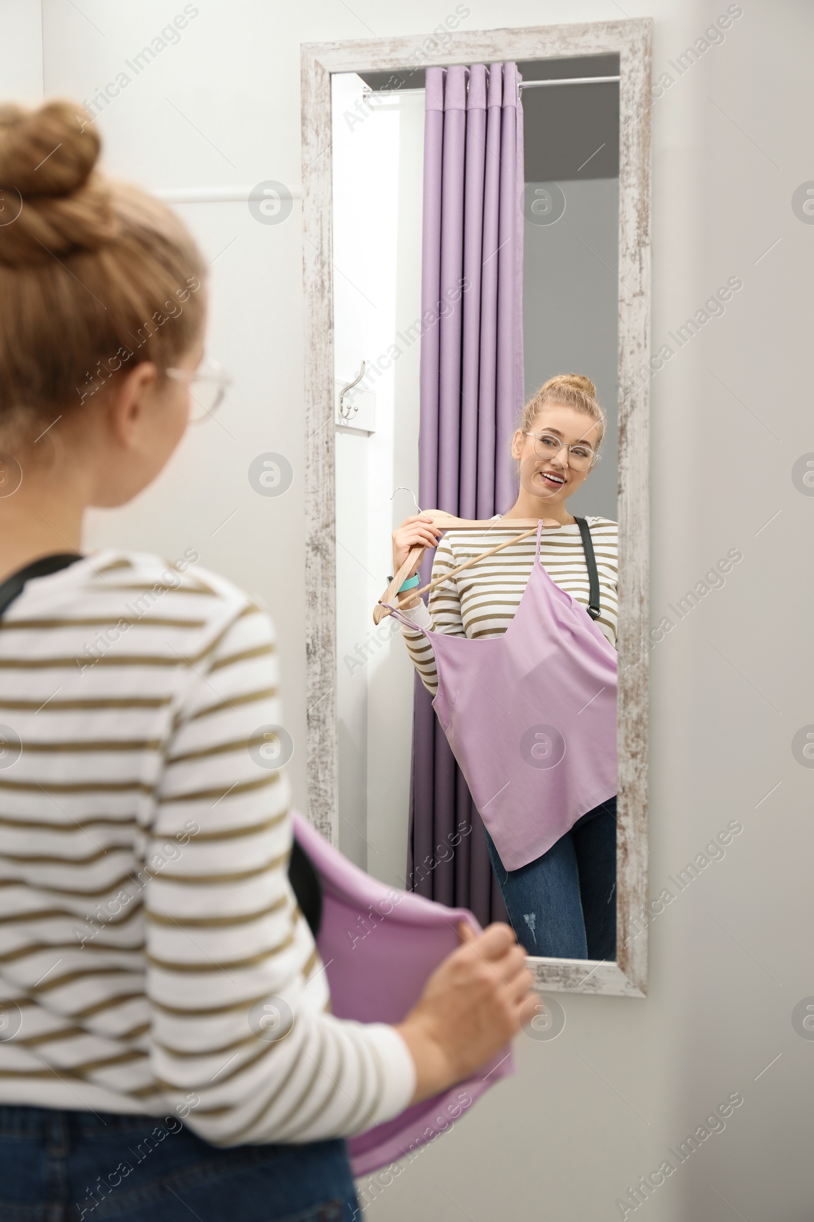 Photo of Young woman with clothes on hanger in dressing room. Fashion store