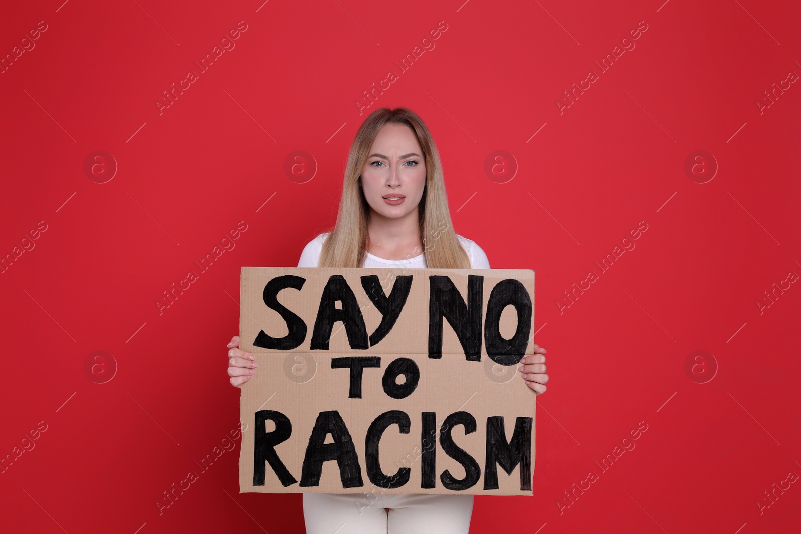 Photo of Young woman holding sign with phrase Say No To Racism on red background